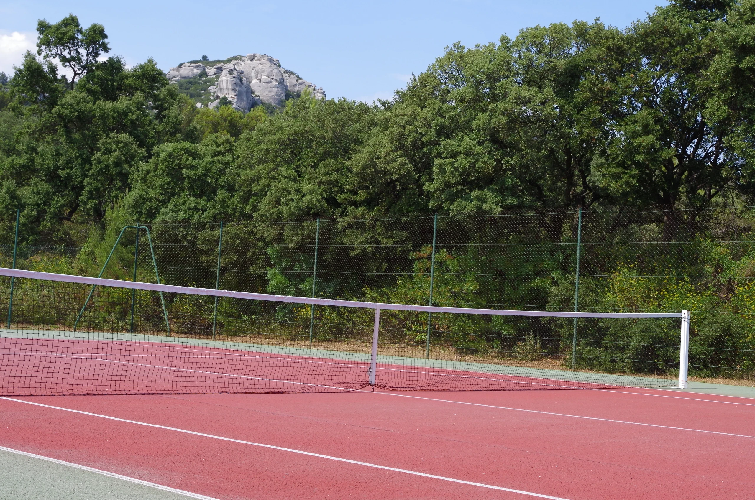Terrain de tennis rouge avec filet et montagne en arrière-plan